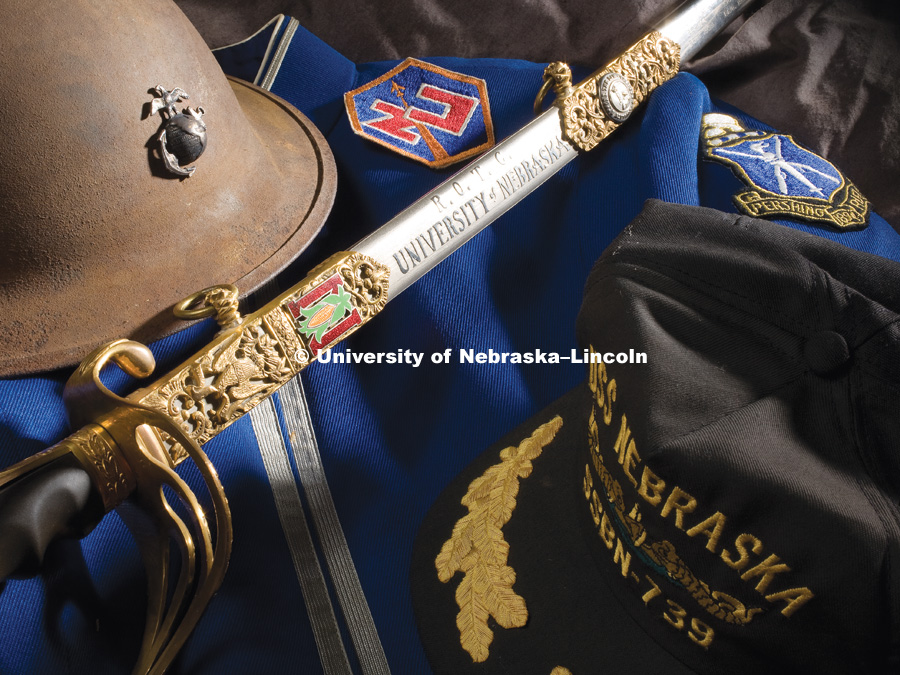 A cadet sword from the 1920s rests on a uniform jacket for the Pershing Rifles drill team.  It is surrounded by a Marine Corp helmet used from 1917 to 1941, an arm patch for the Air Force's Nebraska ROTC cadets and a ballcap from the U.S.S. Nebraska, an Ohio-class ballistic missile submarine named for the state.  All of this is on display in Pershing Hall. Memorabilia for old calendar project. Photo by Craig Chandler/University Communications/University of Nebraska–Lincoln