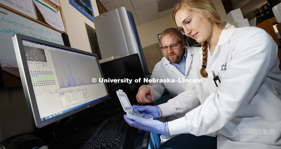 Kara Robbins and Professor Dustin Loy discuss the small sample tray of the new MALDI-TOF. Robbins is validating Moraxella bacteria as part of her undergrad research project. She is using a new device called a MALDI-TOF. It uses a laser to vaporize