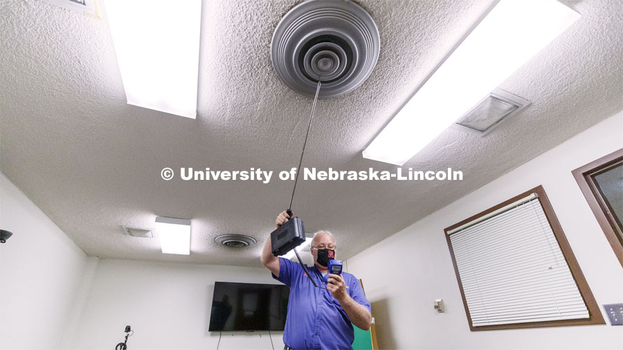 Dave Tyler, Control Systems Tech, uses a hot wire anemometer to measure air coming from a vent in a practice room in Westbrook Music Building. To mitigate the risk of virus transfer within the buildings, the facilities team is increasing by nearly 50 percent the amount of fresh air being drawn into HVAC systems. They are also upgrading filters to more efficiently capture and reduce large and small particles in the air. July 27, 2020. Photo by Craig Chandler / University Communication.