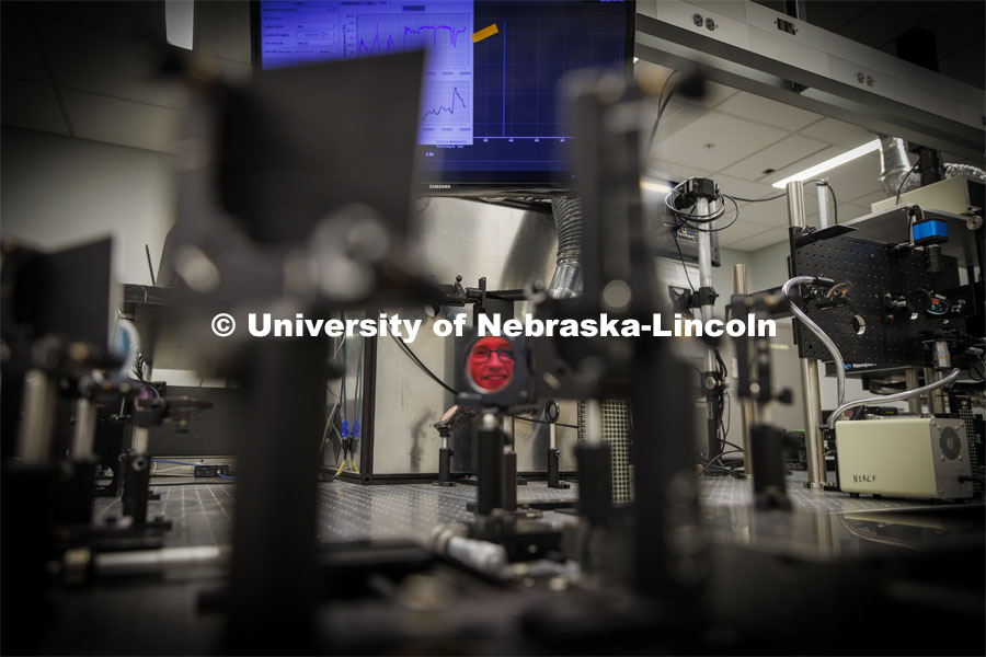 Ben Sukup is reflected in a mirror that is part of the laser system in Craig Zuhlke’s lab. College of Engineering photo shoot. March 22, 2022. Photo by Craig Chandler / University Communication.