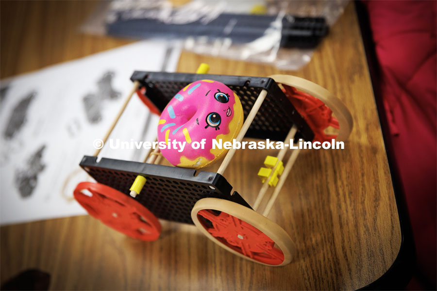 A doughnut squishy decorates a rubber-band powered car. Nebraska honors students Spencer Knight (blue shirt) and Rohan Tatineni (glasses) work with Riley Elementary students in their after-school STEM club. November 22, 2022. Photo by Craig Chandler / University Communication.