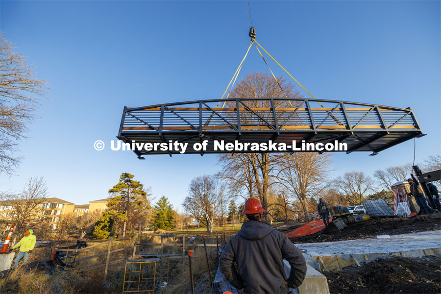 A 40-foot, three-and-a-half-ton bridge is lifted into place over Dead Mans Run on East Campus’ Maxwell Arboretum. December 5, 2023. Photo by Craig Chandler / University Communication and Marketing.