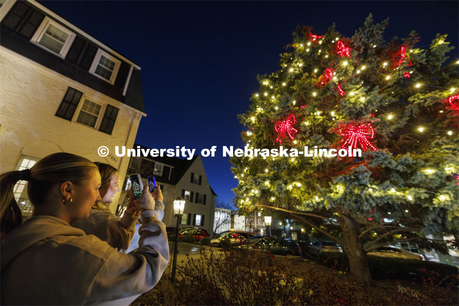 Alpha Phi members Jill Parr, left, and Kamryn Crouch photograph the tree decorated for the holidays outside their sorority house Thursday evening. City Campus. December 7, 2023. Photo by Craig Chandler / University Communication and Marketing.