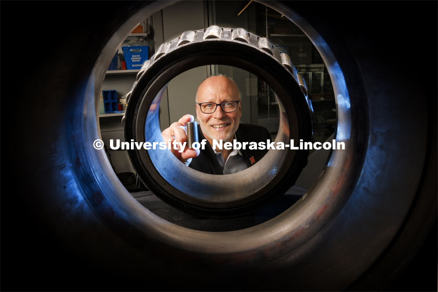 Joe Turner, Professor of Mechanical Engineering, holds a 3-D printed railcar bearing. He is photographed through an actual bearing and housing that fits on the end of each axle of a railcar axle. March 27, 2024. Photo by Craig Chandler / University Communication and Marketing.