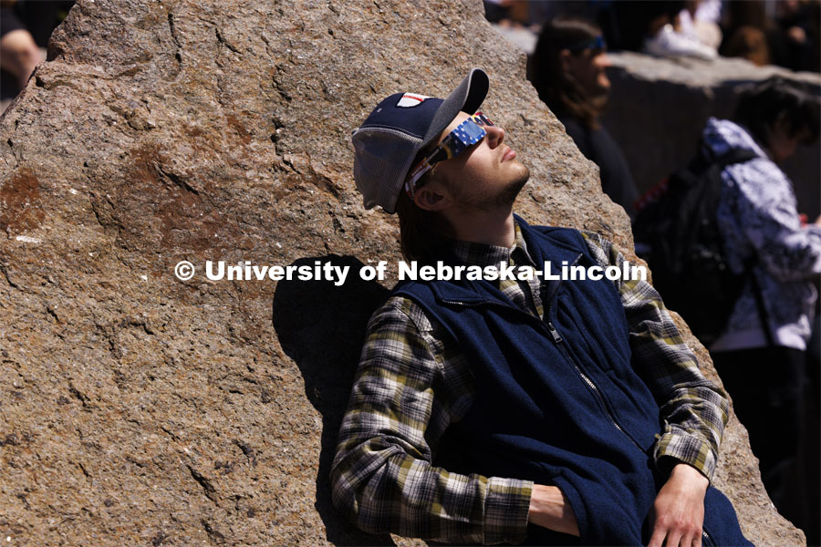 Nathan Benedix leans against the rocks in the Broyhill fountain to watch the eclipse. The Solar Social party to view the partial solar eclipse filled the greenspace outside the Nebraska Union on City Campus. April 8, 2024. Photo by Craig Chandler / University Communication and Marketing.