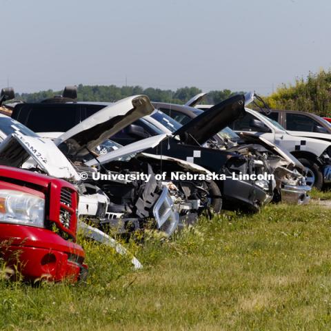 Rows of previous test cars and trucks sit behind the facility. Test of bull-nose barrier for use in medians to protect cars from overpass columns. Test was at university's Midwest Roadside Safety Facility at the Lincoln airport. June 5, 2018. Photo by