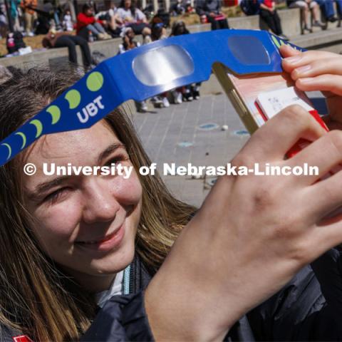 Maria Tamamova uses the eclipse glasses to take a photo with her phone. The Solar Social party to view the partial solar eclipse filled the greenspace outside the Nebraska Union on City Campus. April 8, 2024. Photo by Craig Chandler / University Communication and Marketing.