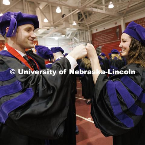 Lucas Zoller and Kat Rosenberger fist bump as they await the ceremony. College of Law commencement in Devaney on the volleyball court. May 3, 2024. Photo by Craig Chandler / University Communication and Marketing.