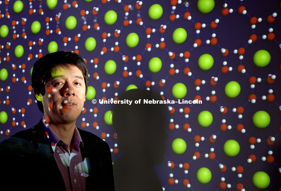Xiao Cheng Zeng, Ameritas University Professor and Willa Cather Emeritus Professor.  He is shown with computer generated renderings of his work behind him. Square-octagon ice clathrate with argon atoms (green) inside octagonal openings is the multi green sphere image. Single-walled Hexagonal Silicon Nanotube. 100331, Photo by Craig Chandler / University Communications
