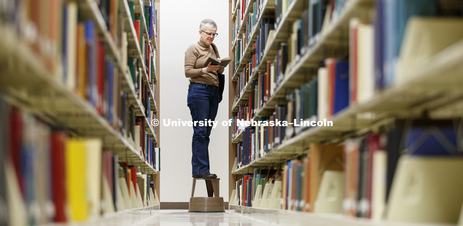 Melissa Homestead, Professor of English, checks out a book from the top shelf of one of the library stacks. The basement of Love Library north filled with hunters looking to document interesting bits of history in handwritten margin notes, photographs and