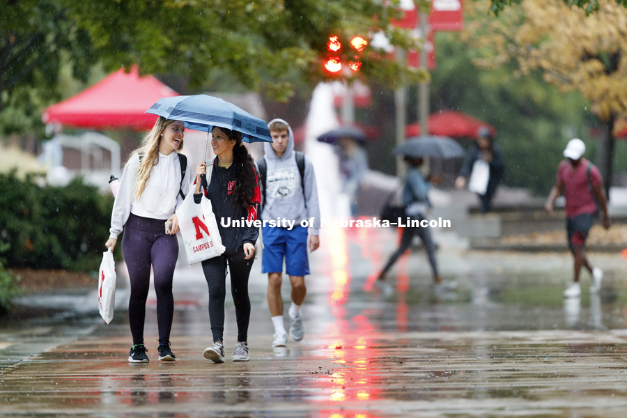Katie Whittaker of Papillion and Gisselle Hernandez of Dakota City, South Dakota, share an umbrella and a conversation on the first day of classes. August 20, 2018. Photo by Craig Chandler / University Communication.