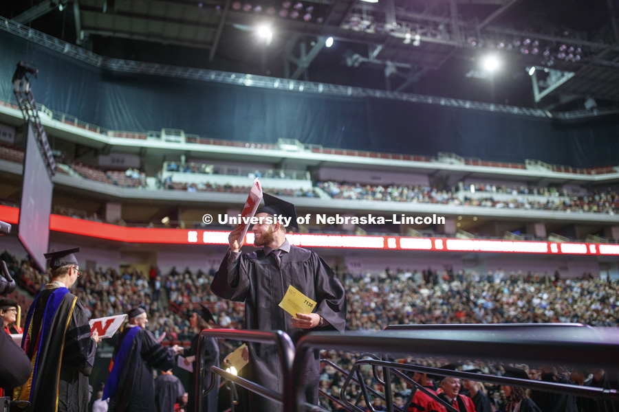 Adam Wainer shows his diploma to family and friends at the Undergraduate Commencement in Pinnacle Bank Arena. December 15, 2018. Photo by Craig Chandler / University Communication.