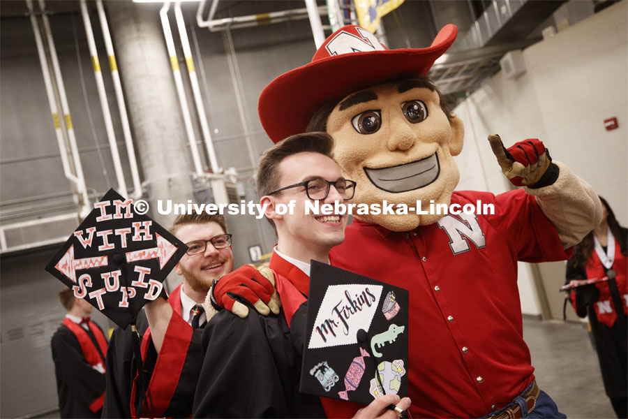 Andrew Firkins is photo bombed (mortar bombed?) by Alexander Crowley as Firkins poses with Herbie Husker before the ceremony. Undergraduate commencement at Pinnacle Bank Arena, May 4, 2019. Photo by Craig Chandler / University Communication.