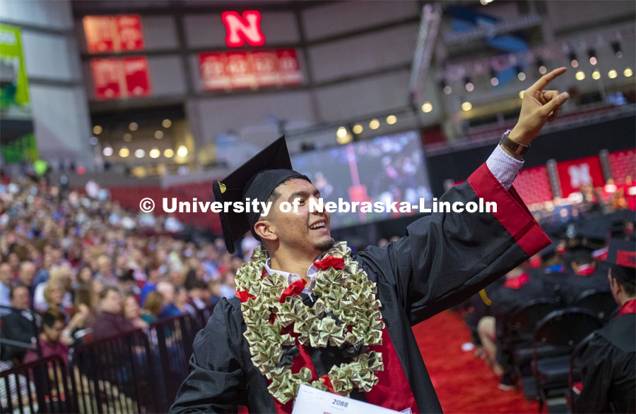 Bertin Jacobo waves to family and friends.  He wore a lei of money to commencement. Undergraduate commencement at Pinnacle Bank Arena, May 4, 2019. Photo by Craig Chandler / University Communication.