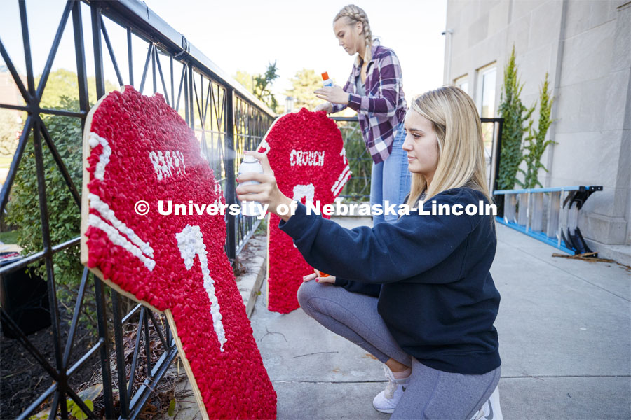 Meghan Arena, sophomore from Omaha, front, and Willa Scoville, freshman from Hartington, NE, spray fixative onto decorated football jerseys outside the Alpha Tau Omega house. Students from Alpha Tau Omega, Gamma Phi Beta, Delta Delta Delta, Acacia, Sigma Alpha Mu work on their display. 2019 Homecoming display decorations. October 3, 2019. Photo by Craig Chandler / University Communication.