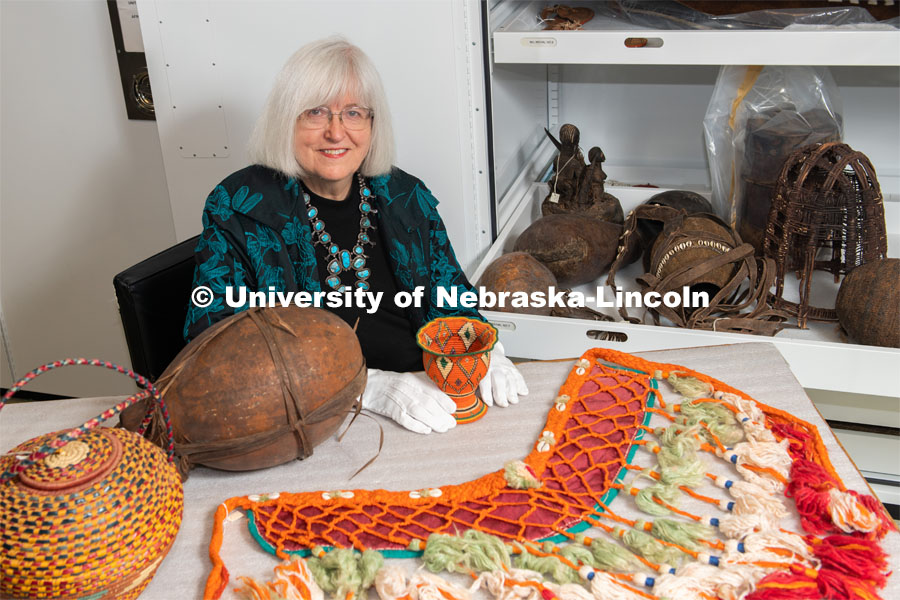 Priscilla Grew, director emerita, admires objects in the University of Nebraska State Museum’s African collection, including a horse breast collar purchased in Egypt. She holds a basket from Ethiopia collected about 1960. Also in the photo are a large basket from Sudan and a gourd from Tanzania. February 26, 2020. Photo by Greg Nathan / University Communication.