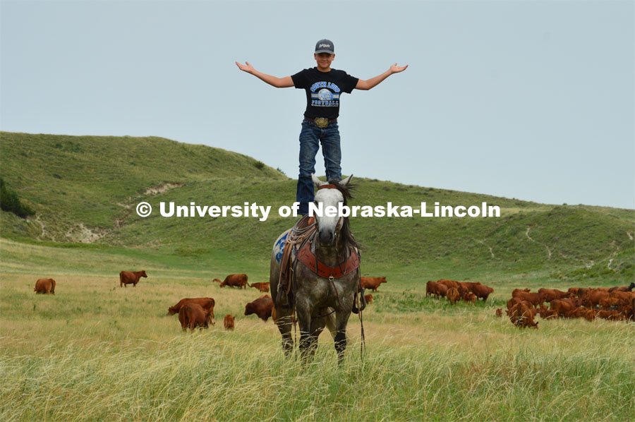 A young rancher shows his skills of standing on the back of his horse. Cattle and livestock on the Diamond Bar Ranch north of Stapleton, NE, in the Nebraska Sandhills. June 23, 2020. Photo by Natalie Jones.  Photos are for UNL use only.  Any outside use must be approved by the photographer.