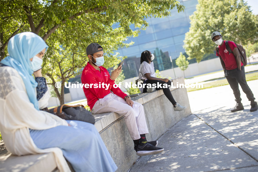 Aldi Airori checks his phone while wearing a mask and practicing social distancing outdoors. Photo shoot of students wearing masks and practicing social distancing. June 24, 2020. Photo by Craig Chandler / University Communication.