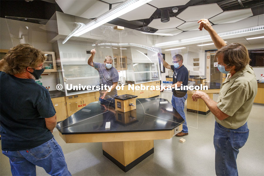 Nebraska's (from left) Mark Thompson, Keith Placek, Jody Redepenning and Pat Pribil lift an acrylic barrier onto a lab table in Hamilton Hall. The barrier is a prototype that is being refined as part of the university’s preparations for a return to on-campus instruction for the fall semester. The barriers will allow chemistry lab tables to be divided into four sections. The barrier is the second prototype and will be refined as part of 78 barriers being manufactured for the beginning of fall classes. Redepenning is chair and professor of chemistry. Thompson, Placek and Pribil are part of the university's Chemistry/Physics and Astronomy Instrument Shop. July 1, 2020. Photo by Craig Chandler / University Communication.