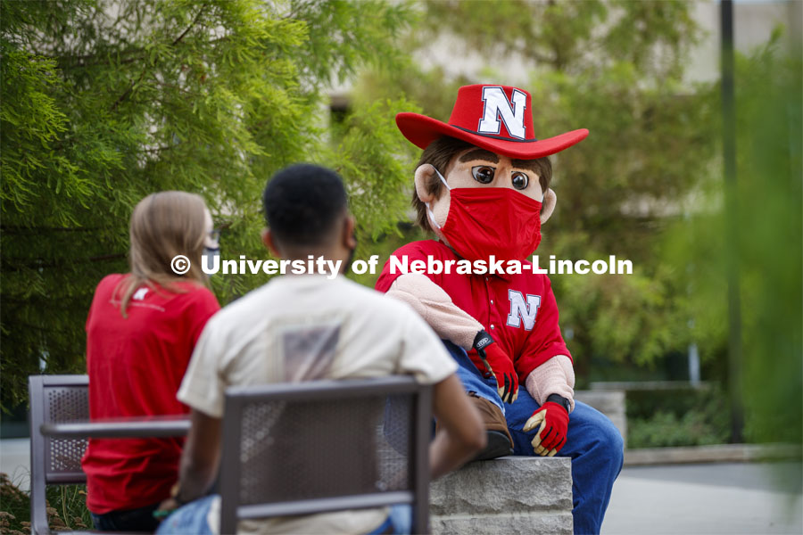 Photo shoot of students with Herbie on city campus display mask wearing, social distancing. Students sitting at tables and hanging out with Herbie Husker. August 5, 2020. Photo by Craig Chandler / University Communication.