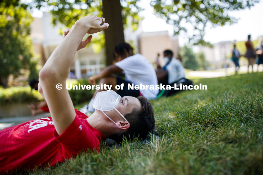 Johnathan O'Keeffe checks his phone while lying in the grass outside of the Woods Art Building before his photography class. First day for in-person learning for the fall semester. August 24, 2020. Photo by Craig Chandler / University Communication.