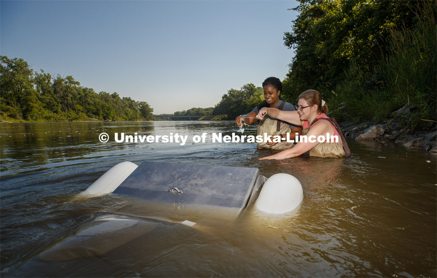 Summer research scholar Moriah Brown from Howard University and Meredith Sutton, graduate student in environmental engineering, attach a flowmeter to a floating sieve to sample water in the Elkhorn River. They are working with Professor Shannon Bartlet-Hunt researching textiles as a source of microplastic fibers to Nebraska streams. July 2, 2021. Photo by Craig Chandler / University Communication.