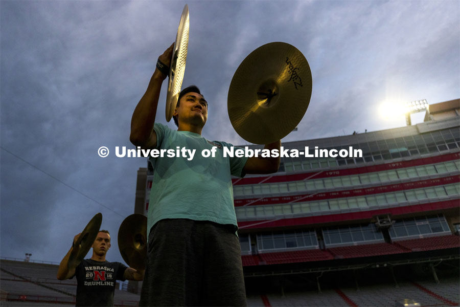 Martin Nguyen’s cymbal reflects the light onto his face as the Cornhusker Marching Band percussion group began the first day of classes at 6:30 am in Memorial Stadium. First day of classes for fall semester. August 23, 2021. Photo by Craig Chandler / University Communication.