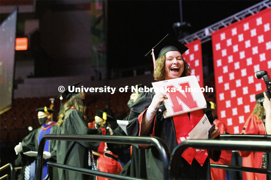 A new grad holds up her diploma and smiles for the camera at the Undergraduate Commencement at Pinnacle Bank Arena. December 18, 2021 Photo by Craig Chandler / University Communication.