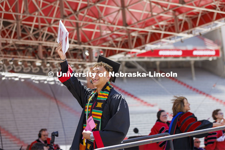 Hunter Johnson holds his diploma up as he walks off the stage so the cameras can show him on the video screen in Memorial Stadium. UNL undergraduate commencement in Memorial Stadium. May 14, 2022. Photo by Craig Chandler / University Communication.