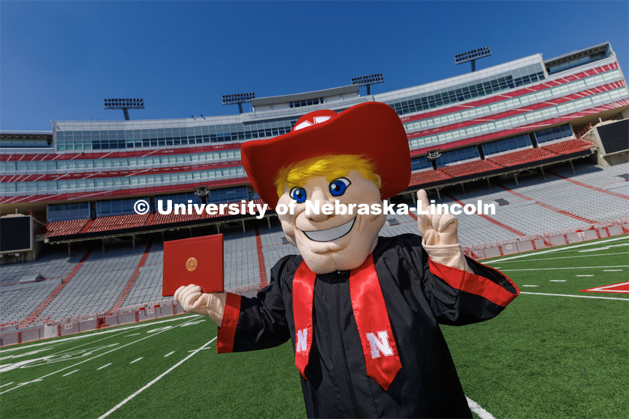 Herbie poses on the field in Memorial Stadium in his graduation regalia. New Herbie photoshoot. April 7, 2023. Photo by Craig Chandler / University Communication.