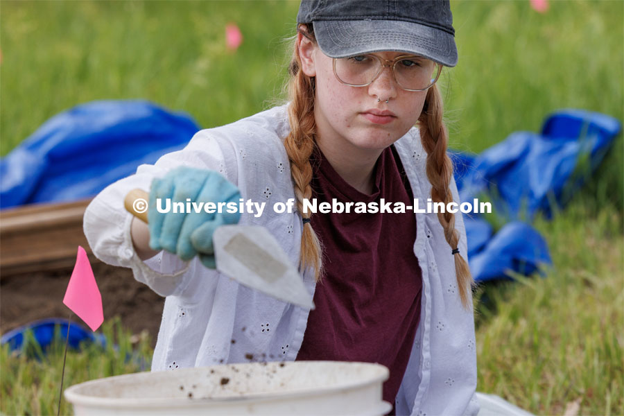 Sophia Huss, sophomore in anthropology, deposits a trowel of soil while excavating a plastic skeleton representing an apparent crime victim at a forensic anthropology site. LuAnn Wandsnider is leading anthropology and forensic anthropology digs at the Reller Prairie in southwest Lancaster County. June 9, 2023. Photo by Craig Chandler / University Communication.