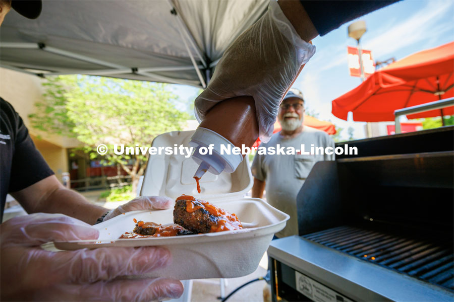 Sean Jones, a line cook with dining services, adds Oklahoma BBQ sauce to Jeff Logans order of ribs and sausages. East Campus Dining’s Summer Grill Outs include Oklahoma BBQ today. July 20, 2023. Photo by Craig Chandler / University Communication.