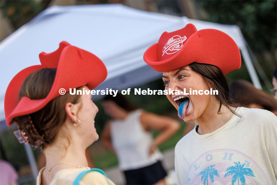 Melanie White of Plainfield, Illinois, shows off her blue tongue from a free sucker while she and her friend wear foam give-away hats. Big Red Welcome Street Fest on the Memorial Stadium loop. Hundreds of clubs and organizations give away stuff to students. August 20, 2023. Photo by Craig Chandler / University Communication.