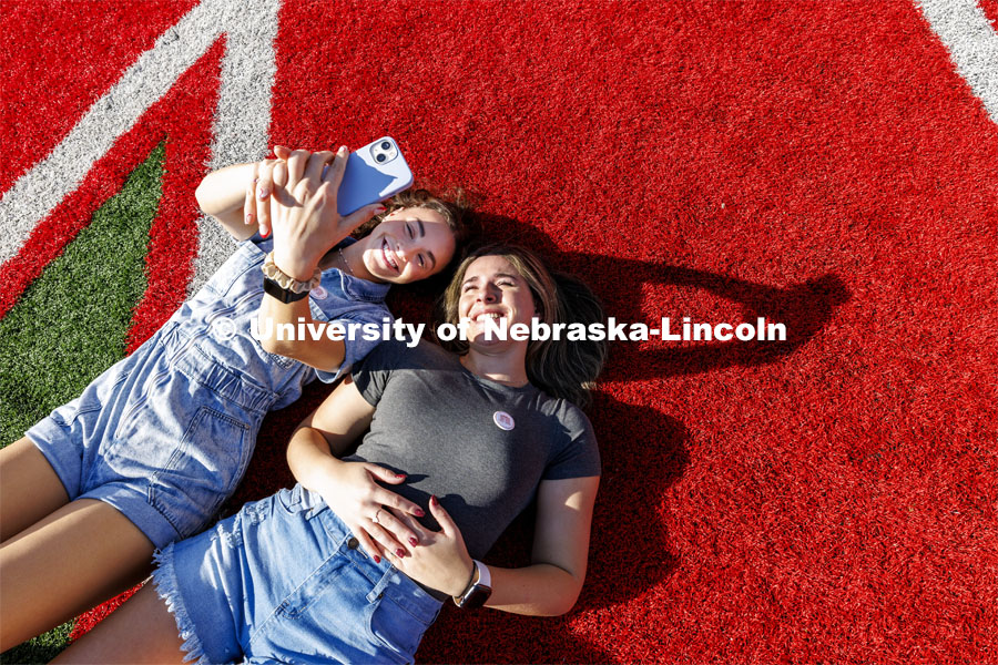 Lydia Storm and Rachel Morros take a selfie on the N in Memorial Stadium during the birthday party. Memorial Stadium 100th birthday party at the stadium. The free public event featured cake and visitors could walk onto the field. October 23, 2023. Photo by Craig Chandler / University Communication.