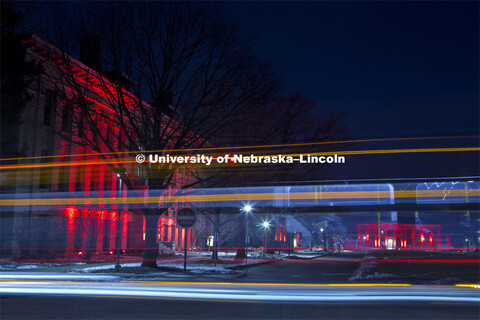 A bus drives by Agriculture Hall during Glow Big. Glow Big Red bathes the campuses with red lights a