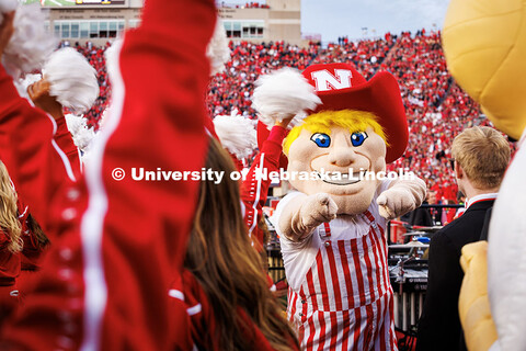Herbie Husker wearing red and white striped overalls points at the camera at the Huskers vs. Wiscons