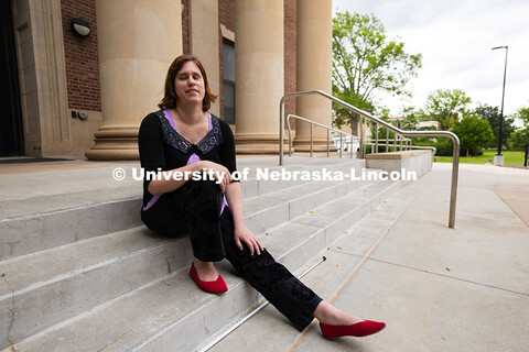 Kelly Coleman is seated on the steps outside of Louise Pound Hall, where she works in Services for S