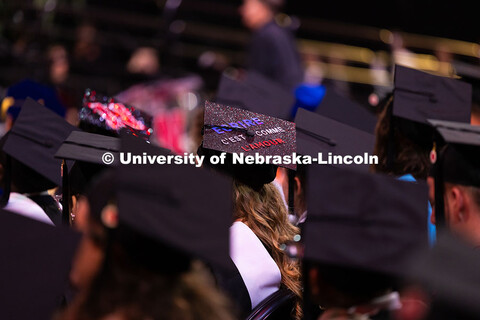 A graduate's cap reads "ecrire c'est comme l'amour" in French. Summer Commencement ceremony in Pinna