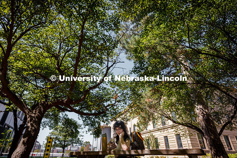 Olivia, a university student, sits on a shaded bench during a sunny afternoon outside of Architectur