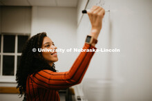 Grad student writing on a marker board in a Louis Pound Hall classroom. April 23, 2019. 