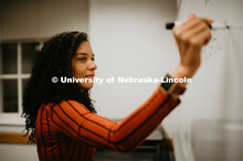 Grad student writing on a marker board in a Louis Pound Hall classroom. April 23, 2019. 