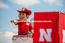 Herbie in a cake on a trailer pointing and waving to children. The University of Nebraska represents
