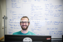 Young man at a computer with a marker board full of equations behind him. Raikes school photo shoot.