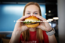 Cather Dining Center photoshoot. Young woman holding a burger in front of her face. March 2, 2020 