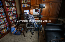 Tyler White records a lecture in his home office while his son, Gavin, 7, plays with their dog Riple