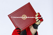 Herbie Husker proudly holds a diploma and is decked out in graduation attire for the Spring Commence