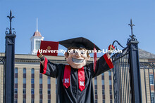Herbie Husker stands in front of Love Library, proudly holding a diploma and is decked out in gradua