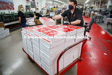 John Tridle stacks a completed Go Big Grad box onto a cart. Printing Service employees work to fill 