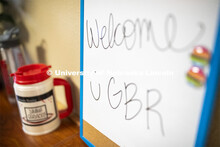White marker board with “Welcome Go Big Red” written on it. Photo shoot of students wearing mask