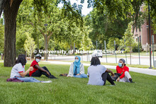 A group of students wearing masks and practice social distancing hangout under a tree on City Campus